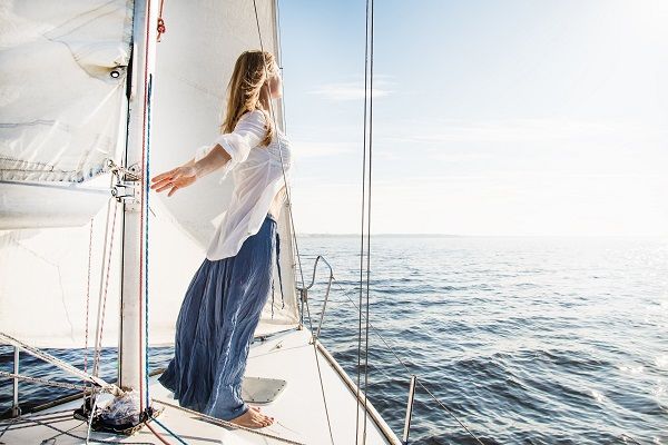 Девушка стоит на яхте в белом платье, раскинув руки в стороны, чувствует себя свободной!